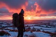 © velikiyzayats - A Young Adult Male Hiker with a Backpack Admiring a Stunning Sunset Over Snow-Covered Fields and Rolling Hills in Winter Landscape