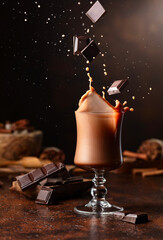 Wall Mural - Pieces of dark chocolate fall into a glass of cocoa drink.