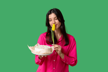 Wall Mural - Beautiful young woman with sweet bento cake and yellow tulip on green background. International Women's Day