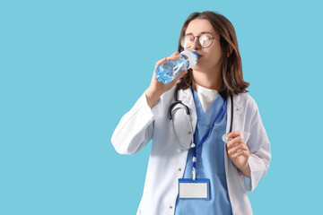 Wall Mural - Female doctor drinking water on blue background