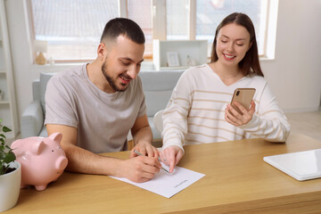 Wall Mural - Young couple with mobile phone filling out refund form at table in room