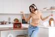 © Pixel-Shot - Young woman with headphones and radio receiver dancing in kitchen