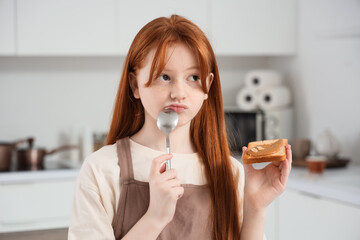 Wall Mural - Thoughtful teenage redhead girl eating toast with nut butter in kitchen, closeup