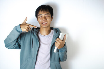 Asian teenager in white t-shirt and blue hoodie, posing pointing at book and smiling