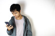 © Fikri - Asian teenager in white t-shirt and blue hoodie, posing focused on looking down at his cellphone