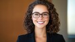 © JAYDA RIN - A professional woman with curly hair and glasses smiles confidently in a business setting, exuding warmth and approachability.