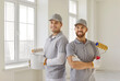 © Studio Romantic - Portrait of smiling happy team of house painters looking at camera with paint rollers and and bucket in hands. Building contractors paint the wall of new apartment doing repair renovation.