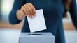 © Blackmint Studio - A person engages in the electoral process by placing a blank ballot into a secure ballot box in a contemporary polling location. The atmosphere is calm and focused