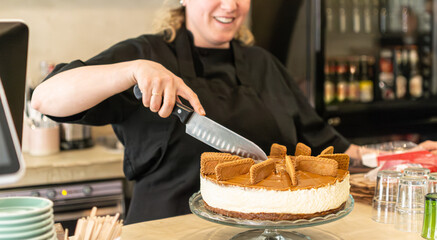 smiling woman cutting caramel cheesecake with a knife in bakery