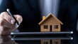© VANATSANUN - Real estate concept with a businessman and a miniature house on a tablet device.