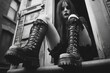© Michael - Young goth woman wearing black leather boots is sitting on a doorstep in an urban environment