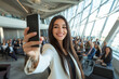 © Gonzalo - Smiling businesswoman taking a selfie at a professional conference, with a large audience in the background inside a modern, well-lit event space with glass windows.