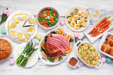 Wall Mural - Classic Easter ham dinner. Overhead view table scene on a white wood background. Ham, scalloped potatoes, vegetable side dishes, eggs, breads and lemon cake dessert.