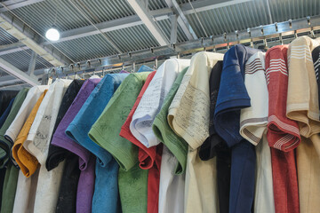 Poster - A rack of colorful shirts with a variety of patterns and designs. The shirts are hanging on a metal rack, and they are all different colors and styles. Scene is cheerful and vibrant
