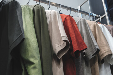 Poster - A rack of shirts with a variety of colors and styles. The shirts are hanging on a rack, and the colors include green, blue, red, and white. Scene is casual and relaxed