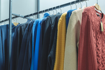 Poster - A rack of clothes with a blue sweater on top. There are many different colors and styles of clothing, including a red sweater, a yellow sweater, and a black sweater. The clothes are neatly hung up