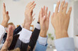 © Studio Romantic - Closeup of business people hands raising hands to vote at the conference standing in meeting room. Company employees in formal clothes men and women voting in office during a meeting