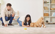 © Studio Romantic - Happy family couple enjoys training and playing with dog at home, using toys to teach the animal. They spend quality time together, engaging in fun activities and strengthening bond.
