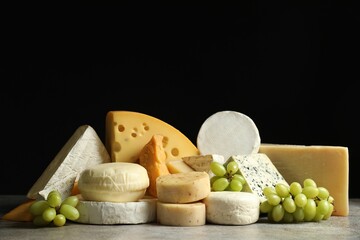 Wall Mural - Different types of cheese and grapes on grey table against black background