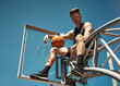© peopleimages.com - Basketball court, sports and portrait of man on net in outdoors park for match, competition and game. Blue sky, happy and person on hoop for goal, score and practice in training, fitness and exercise
