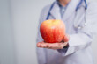 © R Photography - A male doctor stands holding an apple against a white background, promoting healthy eating educates patients on nutrition, wellness, disease prevention through a balanced diet and medical expertise