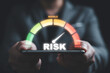© Dilok - Businessman holding smartphone with  risk level indicator rating since low to high for Risk management and assessment concept.