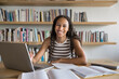© fizkes - Portrait of schoolgirl do homework in library. Excellent student posing for camera with contented smile seated at desk with laptop and textbooks, enjoy effective e-learning using educational platform