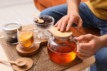 Wall Mural - Young man with glass teapot on table at home, closeup