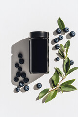 Wall Mural - Elevated Blueberry Elixir: A sleek black container, encircled by a vibrant cascade of fresh blueberries and a sprig of lush greenery, casts a delicate shadow on the scene.