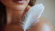 © savittree - Close-up shot of a white feather brushing against a woman bare shoulder, symbolizing tenderness and sensitive skin