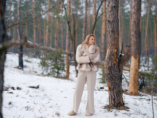 Young woman walking in winter forest near pine trees.