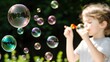 © pattaphorn - Child Blowing Iridescent Soap Bubbles Outdoors on Sunny Day