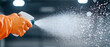 © Wittawit - person wearing orange gloves sprays cleaning solution, creating mist in mid air. image captures action of cleaning, emphasizing hygiene and safety