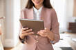 © fizkes - Cropped close up shot female employee dressed in jacket holding digital tablet, working on-line, review presentation, digital content, reports or data, stay connected and productive in modern office