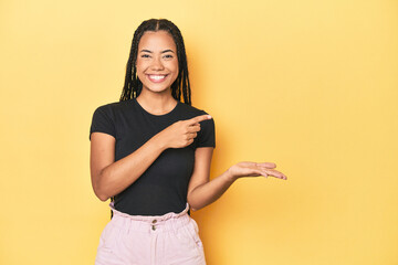 Wall Mural - Young Indonesian woman on yellow studio backdrop excited holding a copy space on palm.