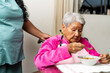 © Guillermo Spelucin - Nurse assisting elderly woman eating soup at home
