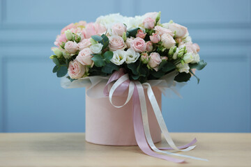 Poster - Gift box with bouquet of beautiful flowers and eucalyptus branches on wooden table against light blue wall