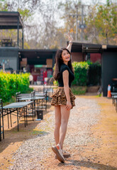 Wall Mural - A cute smiling woman wearing a black dress and a tiger-print skirt in an outdoor cafe.