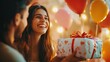 © Joni graphic - A woman happily giving a wrapped gift to her partner, with a festive backdrop of balloons, cake, and streamers, shot with soft-focus lighting for a dreamy effect