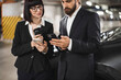 © sofiko14 - Caucasian man and woman in formal attire using smartphones in parking garage, conveying concept of modern business and technology.