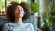 © Pat J. - A calm young woman in casual attire, seated on a grey armchair in a sleek living room, listening to music through headphones with closed eyes, showcasing relaxation