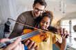 © NDABCREATIVITY - Music is so much fun. Young father teaching his little daughter to play violin and smiling.