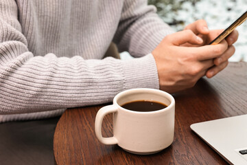 Wall Mural - Man with smartphone having coffee break at wooden table in cafe, closeup