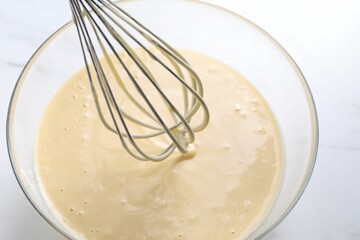 Wall Mural - Whisk and bowl of dough on white table, above view