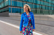 © Westend61 - Woman in colorful dress and blue jacket strolling in urban setting