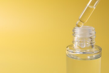 Wall Mural - Dripping serum from pipette into bottle on yellow background, closeup. Space for text