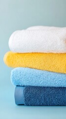 A stack of folded towels in different colors: white, yellow, and blue, against a light blue background