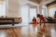 © qunica.com - Two cheerful young girls in colorful outfits enjoy playing on the hardwood floor of a sunlit living room, capturing the essence of fun and childhood friendship.