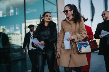 Wall Mural - Young professionals carrying documents, engaging in conversation outside a modern urban office building on a sunny day, emphasizing collaboration, style, and business interaction. The atmosphere