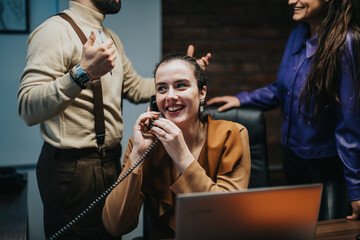 Wall Mural - A cheerful businesswoman converses on the phone while her colleagues interact in a vibrant workplace.